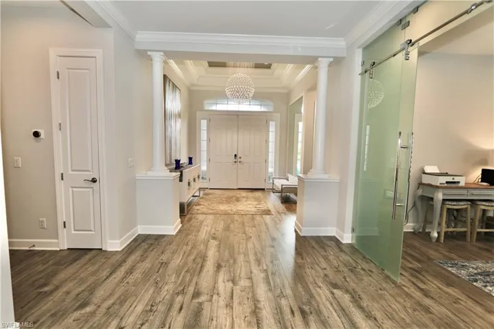 Foyer with a tray ceiling, crown molding, dark wood-style flooring, and suspended lighting