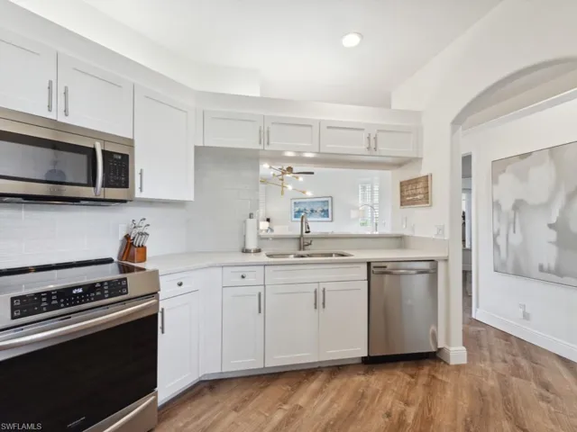 Kitchen with  wood-style flooring, white cabinetry, glass tile backsplash, sink, and appliances with stainless steel finishes