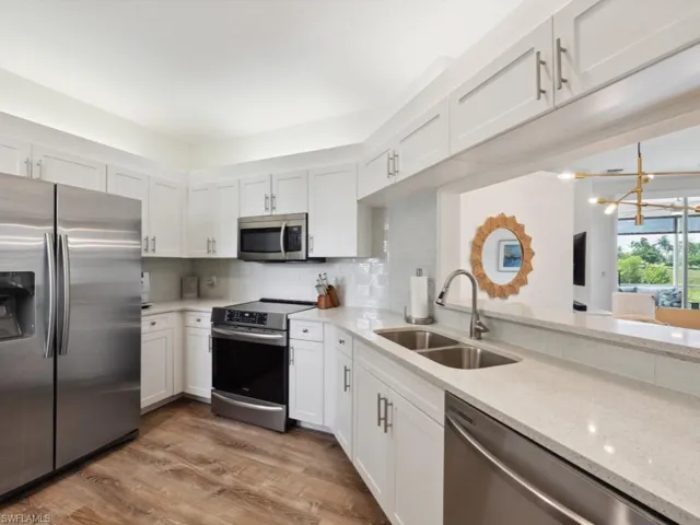 Kitchen with wood-style flooring, a custom chandelier, appliances with stainless steel finishes, sink, and light stone counters