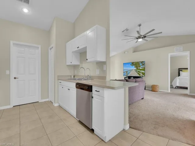 Kitchen featuring white cabinets, dishwasher, light colored carpet, light tile patterned flooring, and vaulted ceiling