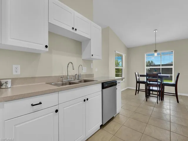 Kitchen featuring light countertops, white cabinetry, stainless steel dishwasher, hanging light fixtures, and light tile patterned flooring