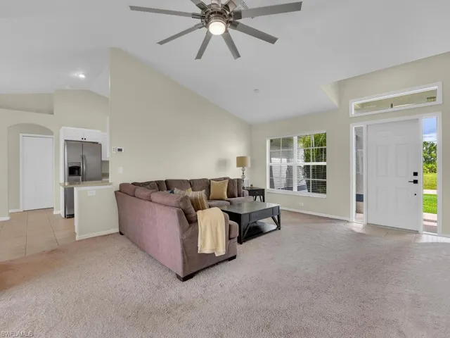 Living room featuring light carpet, light tile patterned floors, ceiling fan, high vaulted ceiling, and arched walkways