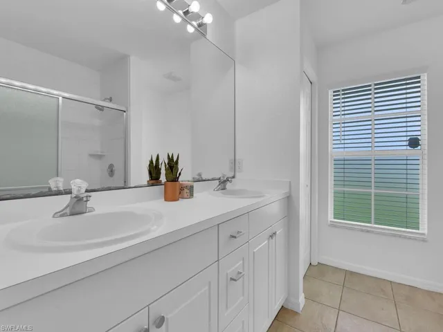 Bathroom featuring a shower stall, double vanity, and light tile patterned floors