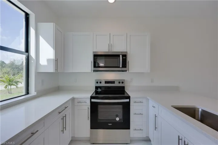 Kitchen with stainless steel appliances, white cabinetry, and light stone counters