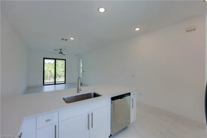 Kitchen with stainless steel dishwasher, light stone countertops, white cabinets, recessed lighting, and ceiling fan