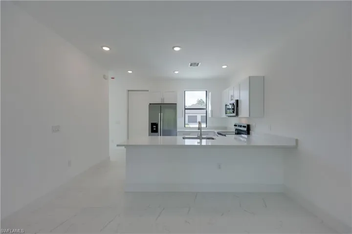Kitchen with stainless steel appliances, a peninsula, white cabinets, recessed lighting, and light stone counters