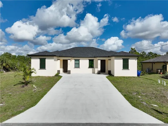 View of front of house with stucco siding, a front yard, concrete driveway, and roof with shingles