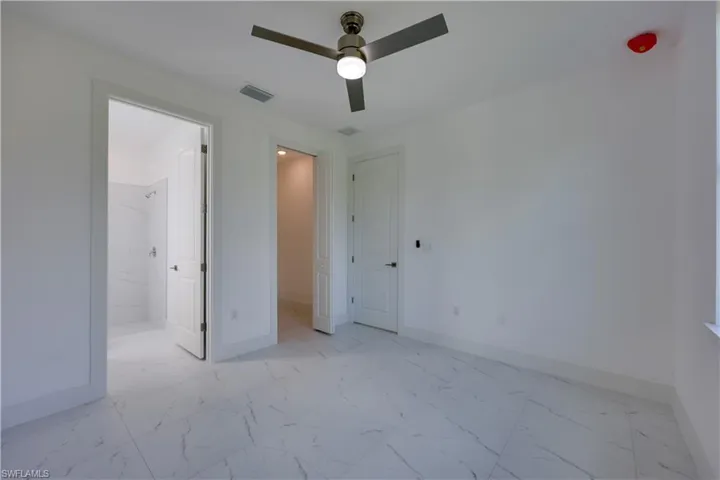 Unfurnished bedroom featuring light marble finish flooring, a ceiling fan, and ensuite bathroom