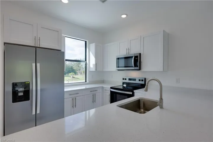 Kitchen featuring stainless steel appliances, light stone counters, white cabinets, and recessed lighting