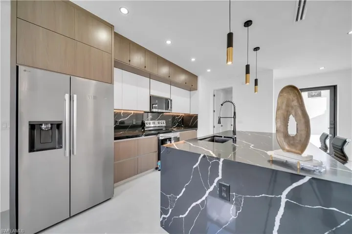 Kitchen featuring stainless steel appliances, decorative light fixtures, dark stone counters, backsplash, and two tone color scheme