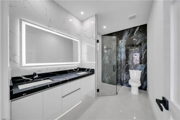 Full bath featuring double vanity, stone wall, a marble finish shower, recessed lighting, and tile walls