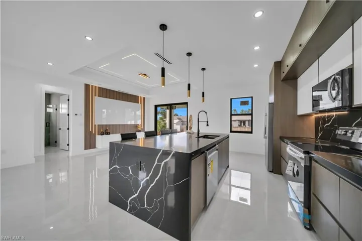 Kitchen featuring stainless steel appliances, a spacious island, dark stone counters, modern cabinets, and hanging light fixtures