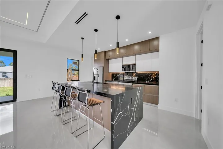Kitchen with dark stone counters, a large island with sink, a breakfast bar area, decorative light fixtures, and stainless steel appliances