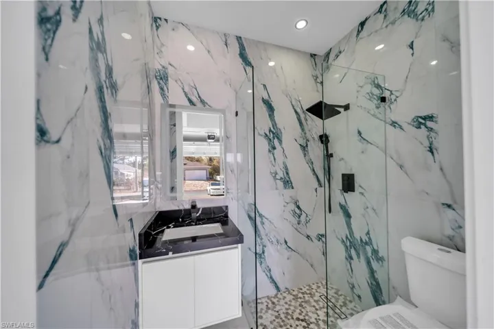 Full bathroom featuring vanity, a marble finish shower, recessed lighting, and stone wall
