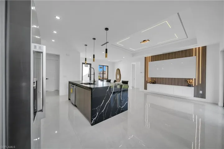 Kitchen with a kitchen island with sink, dark stone countertops, modern cabinets, hanging light fixtures, and stainless steel dishwasher