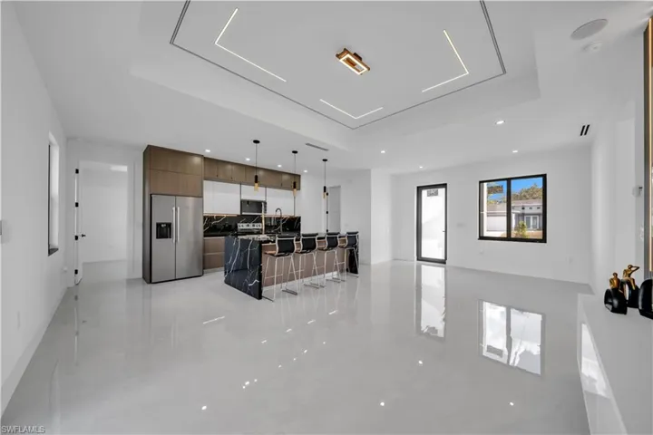 Kitchen with open floor plan, a center island with sink, stainless steel appliances, a raised ceiling, and decorative light fixtures