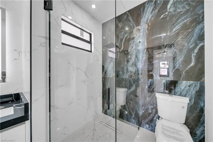 Bathroom with stone wall, a marble finish shower, recessed lighting, and tile walls