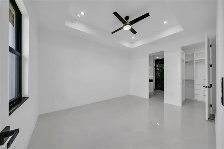 Unfurnished bedroom featuring a walk in closet, recessed lighting, a ceiling fan, and a raised ceiling