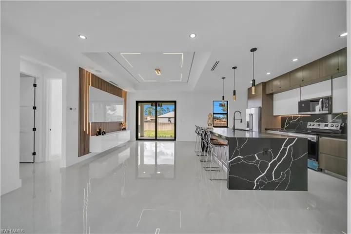 Kitchen featuring dark stone countertops, a raised ceiling, a large island, stainless steel appliances, and a breakfast bar