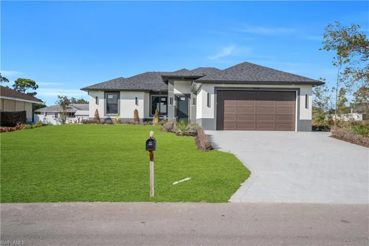 Prairie-style house with stucco siding, decorative driveway, a garage, and a front lawn