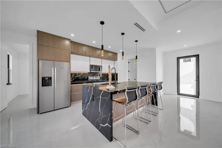 Kitchen with stainless steel appliances, dark stone countertops, a kitchen breakfast bar, an island with sink, and pendant lighting