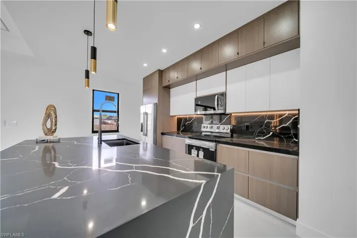 Dual tone kitchen featuring decorative light fixtures, dark stone counters, stainless steel appliances, decorative backsplash, and two tone cabinetry