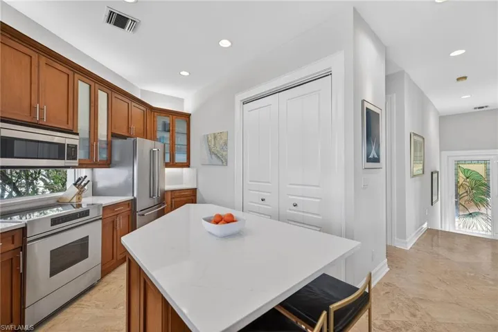 Kitchen featuring stainless steel appliances, wood finish cabinetry, a center island, glass insert cabinets, and a kitchen bar