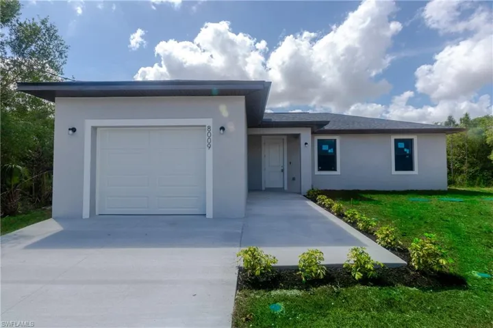 Single story home featuring a garage, a front lawn, stucco siding, and concrete driveway