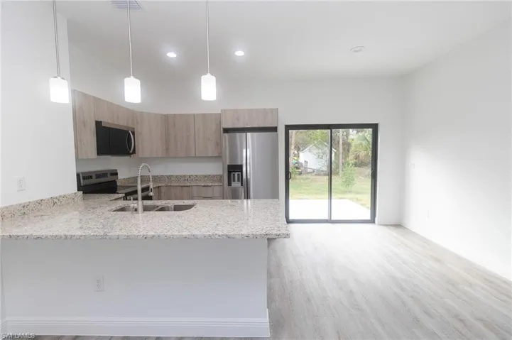 Kitchen with light stone counters, stainless steel appliances, a sink, modern cabinets, and a peninsula