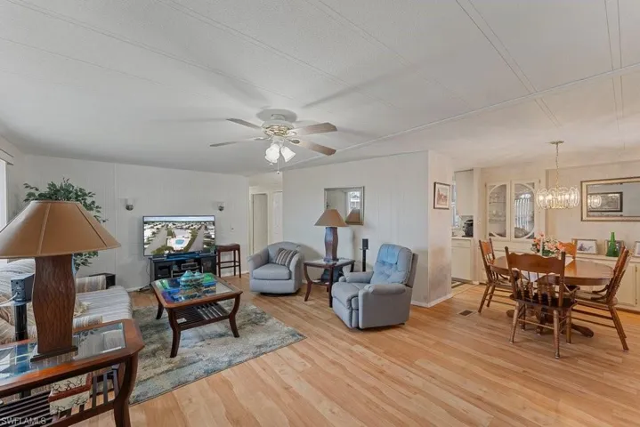 Living room featuring ceiling fan with notable chandelier and light hardwood / wood-style floors