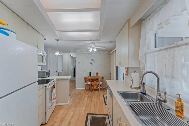 Kitchen with white cabinetry, sink, hanging light fixtures, white appliances, and light wood-type flooring
