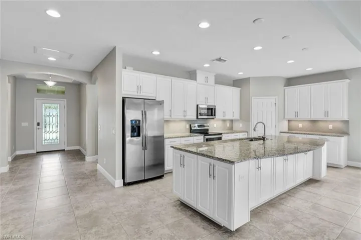 Kitchen featuring appliances with stainless steel finishes, decorative backsplash, white cabinetry, granite countertops, and a Large kitchen island with sink, lots of lighting.