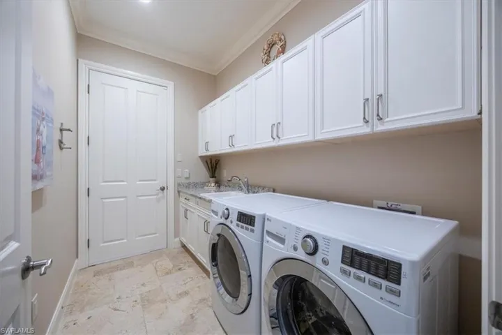 Laundry area featuring ornamental molding, washing machine and clothes dryer, cabinet space, and light stone finish floors