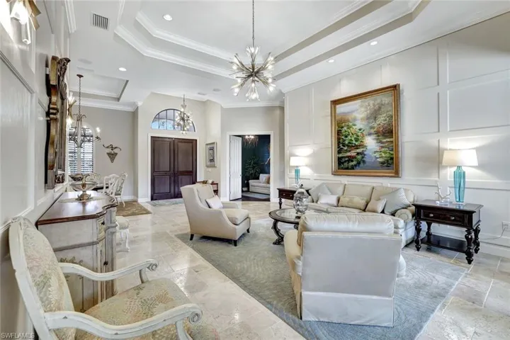 Living room featuring ornamental molding, a chandelier, a decorative wall, recessed lighting, and a raised ceiling