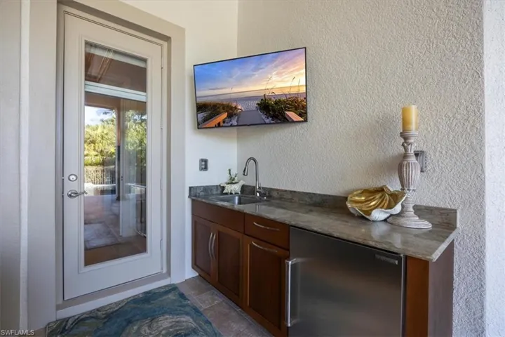 Outdoor wet bar featuring a textured wall, stainless steel fridge, and dark stone countertops