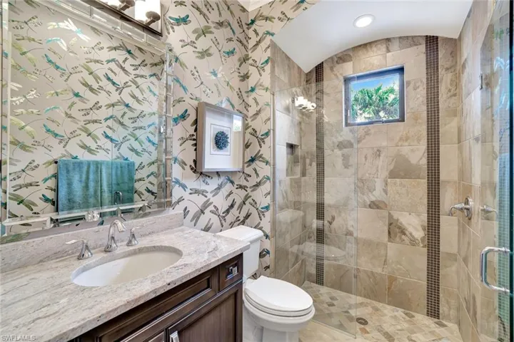 Bathroom featuring wallpapered walls, vanity, and a stall shower