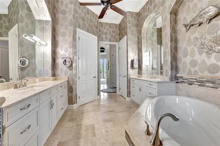 Bathroom with two vanities, a garden tub, a ceiling fan, crown molding, and wallpapered walls
