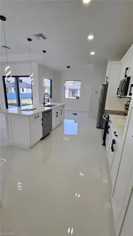 Kitchen featuring white cabinets, pendant lighting, stainless steel appliances, and light stone countertops