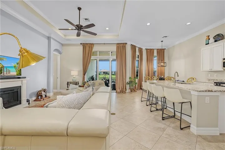 Tiled living room featuring a raised ceiling, crown molding, sink, and ceiling fan