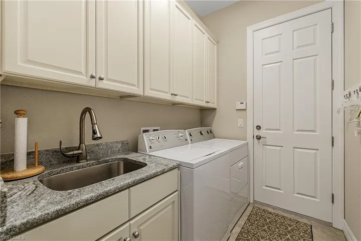 Laundry room featuring light tile patterned flooring, cabinets, washer and dryer, and sink