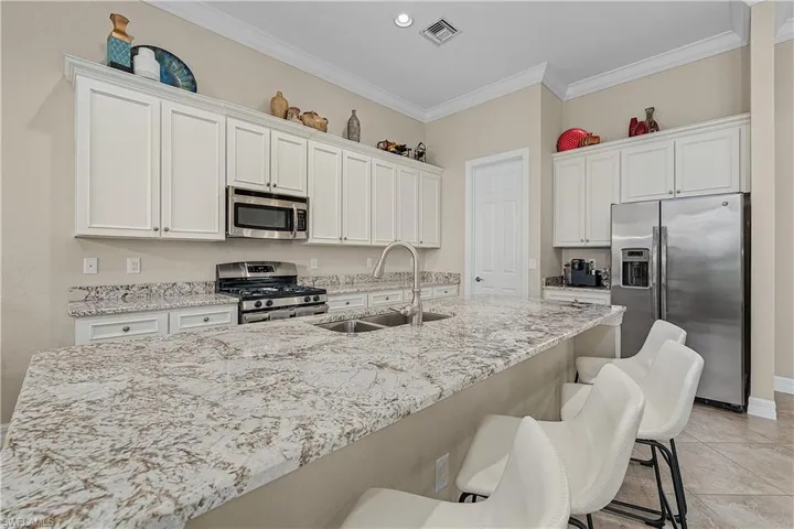 Kitchen featuring white cabinets, sink, a kitchen bar, appliances with stainless steel finishes, and light tile patterned floors