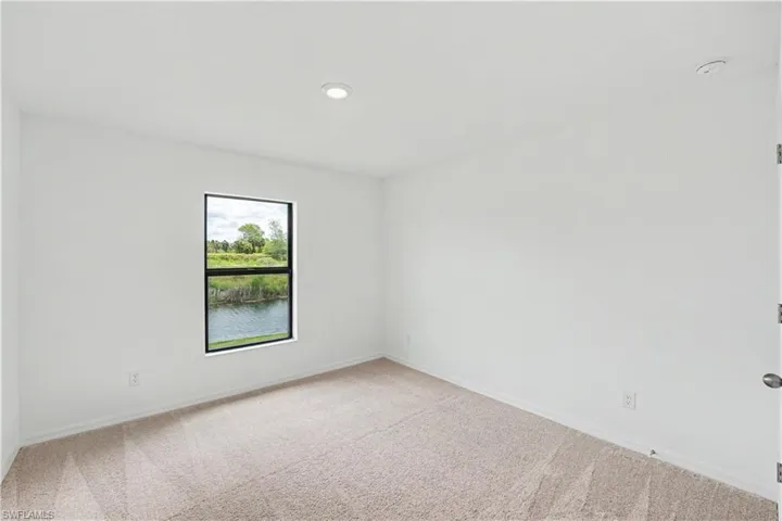 Neutral-toned carpeted room featuring a single window with black trim overlooking a body of water and distant greenery