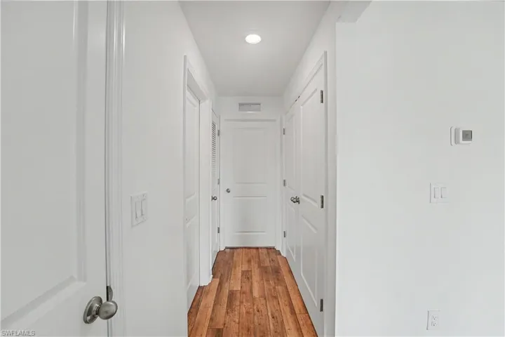 Hallway featuring wood-finish flooring, white walls, recessed lighting, and multiple panel doors with brushed nickel hardware