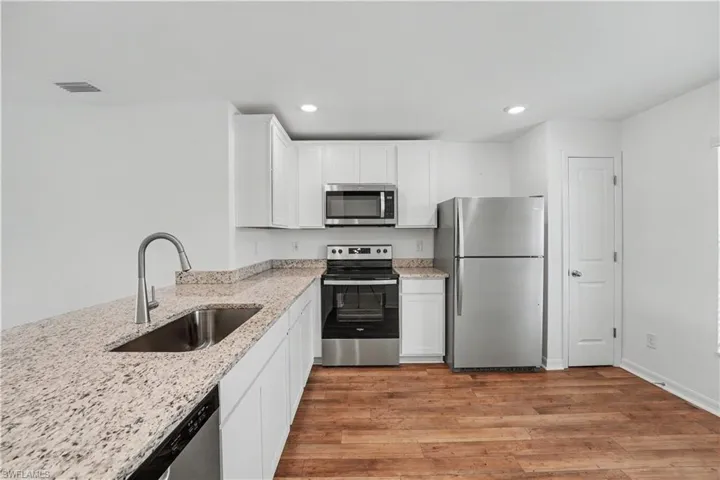 Modern kitchen featuring stainless steel appliances, white cabinetry, speckled countertops, wood-finish flooring, and recessed lighting