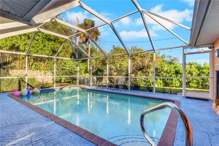Screen-enclosed swimming pool featuring a brick-paver border and concrete decking