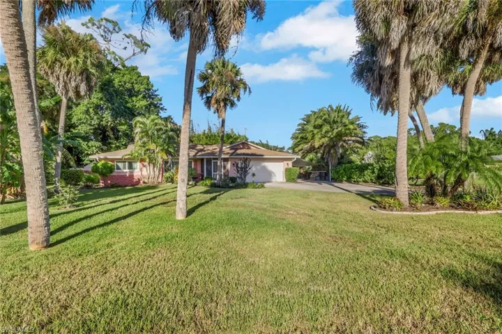 Single-story exterior featuring a brick facade, integrated garage, expansive lawn, and mature palm trees