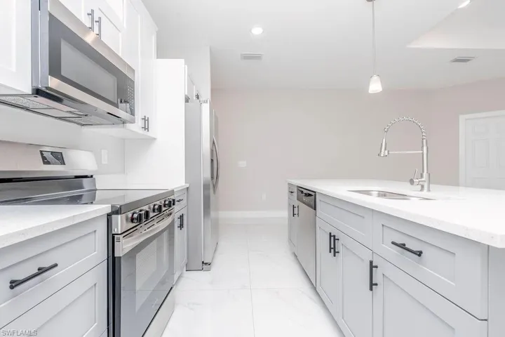 Kitchen featuring stainless steel appliances, pendant lighting, light stone counters, white cabinets, and light marble finish floors