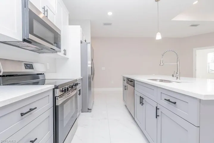 Kitchen featuring stainless steel appliances, light stone countertops, pendant lighting, recessed lighting, and gray cabinetry