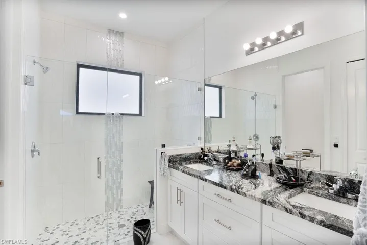 Primary bathroom featuring a shower with shower door, large vanity, and dual sinks