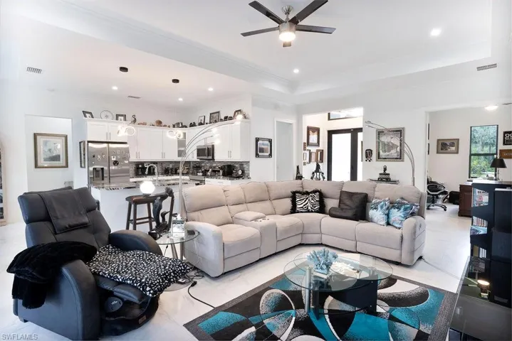 Living room with light tile flooring, ceiling fan, a raised ceiling, and crown molding